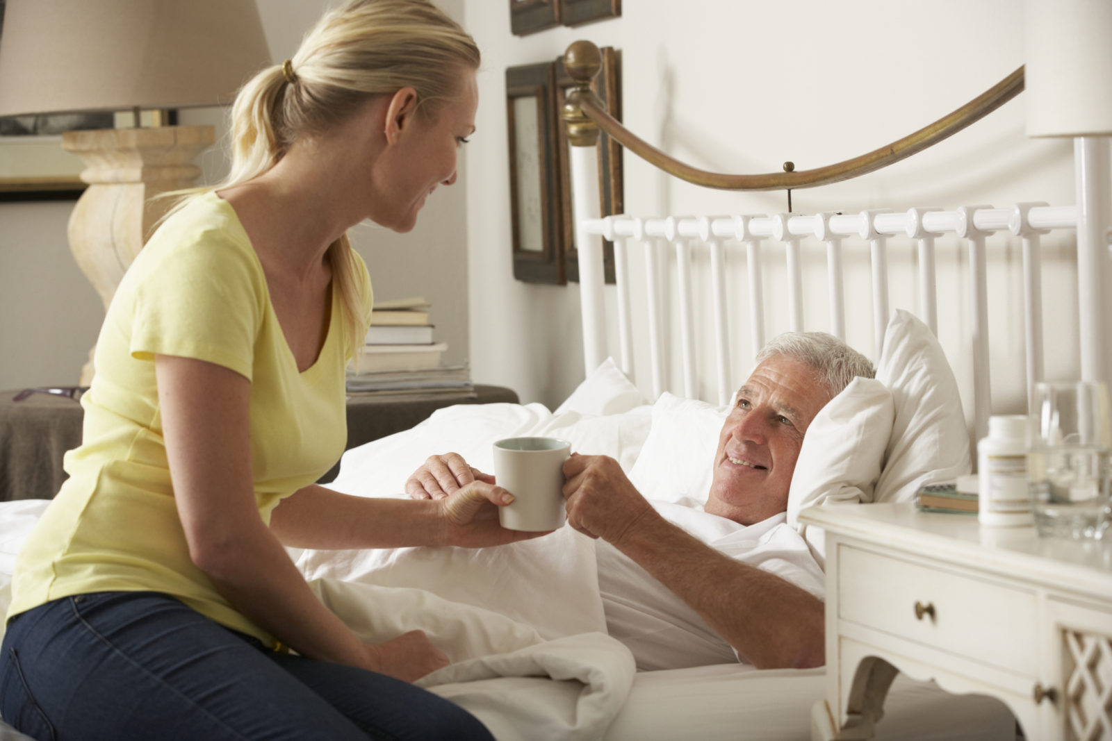 Home caregiver giving a cup of tea to elderly male patient