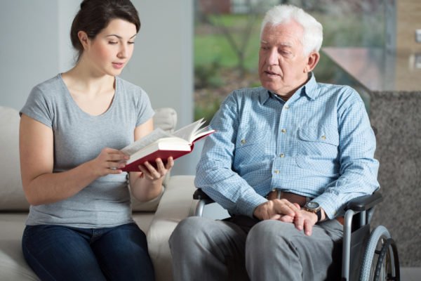 Hospice volunteer reading a book to elderly male patient