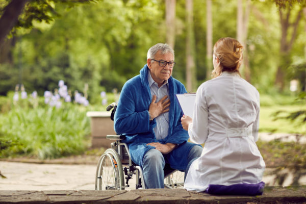 Hospice nurse with elderly man in wheelchair outdoors